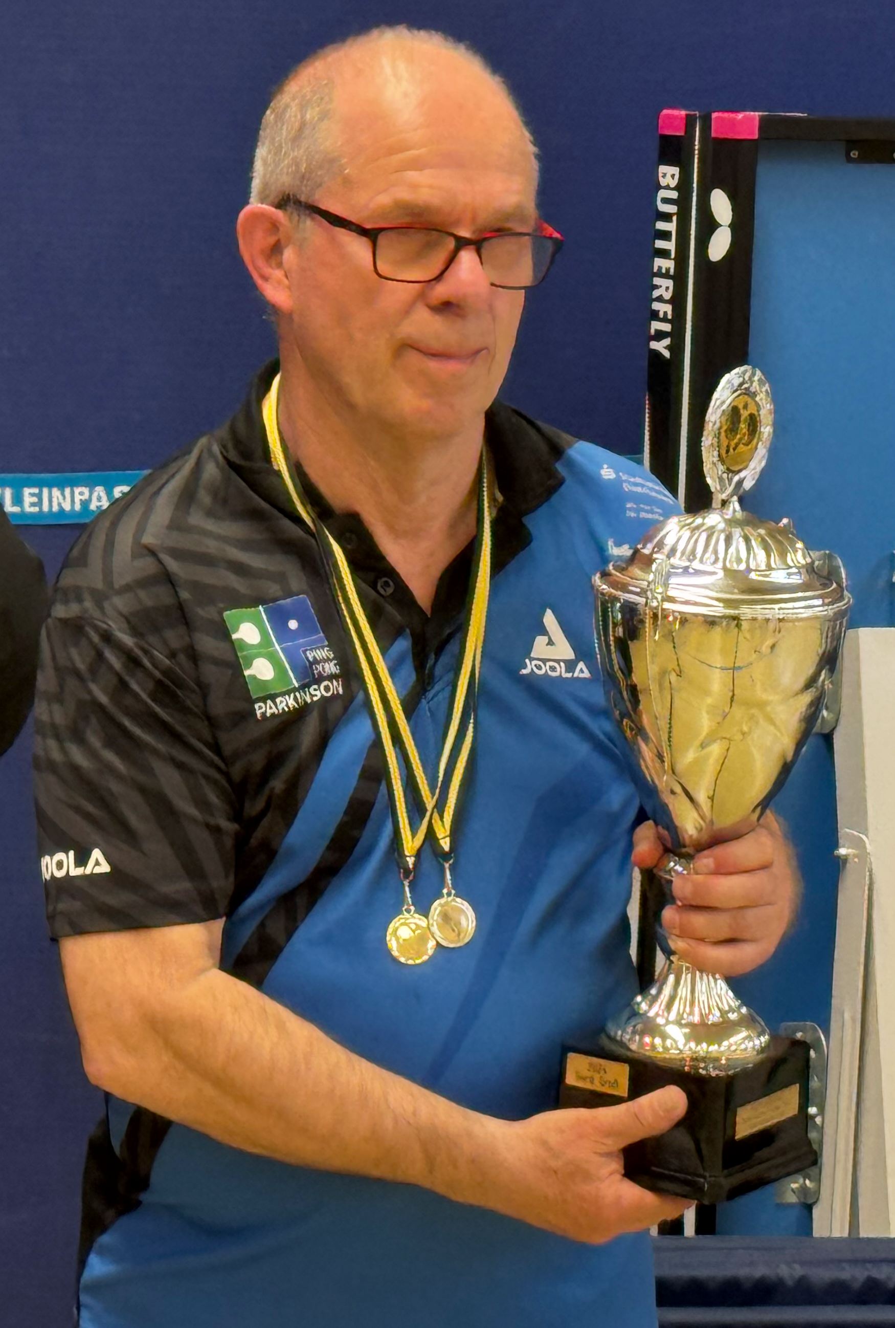 Der Spieler des SC Buschhausen Ede Schunk hält einen gewonnen Siegerpokal in den Händen und trägt weitere 2 Gewinnermedaillen um den Hals.